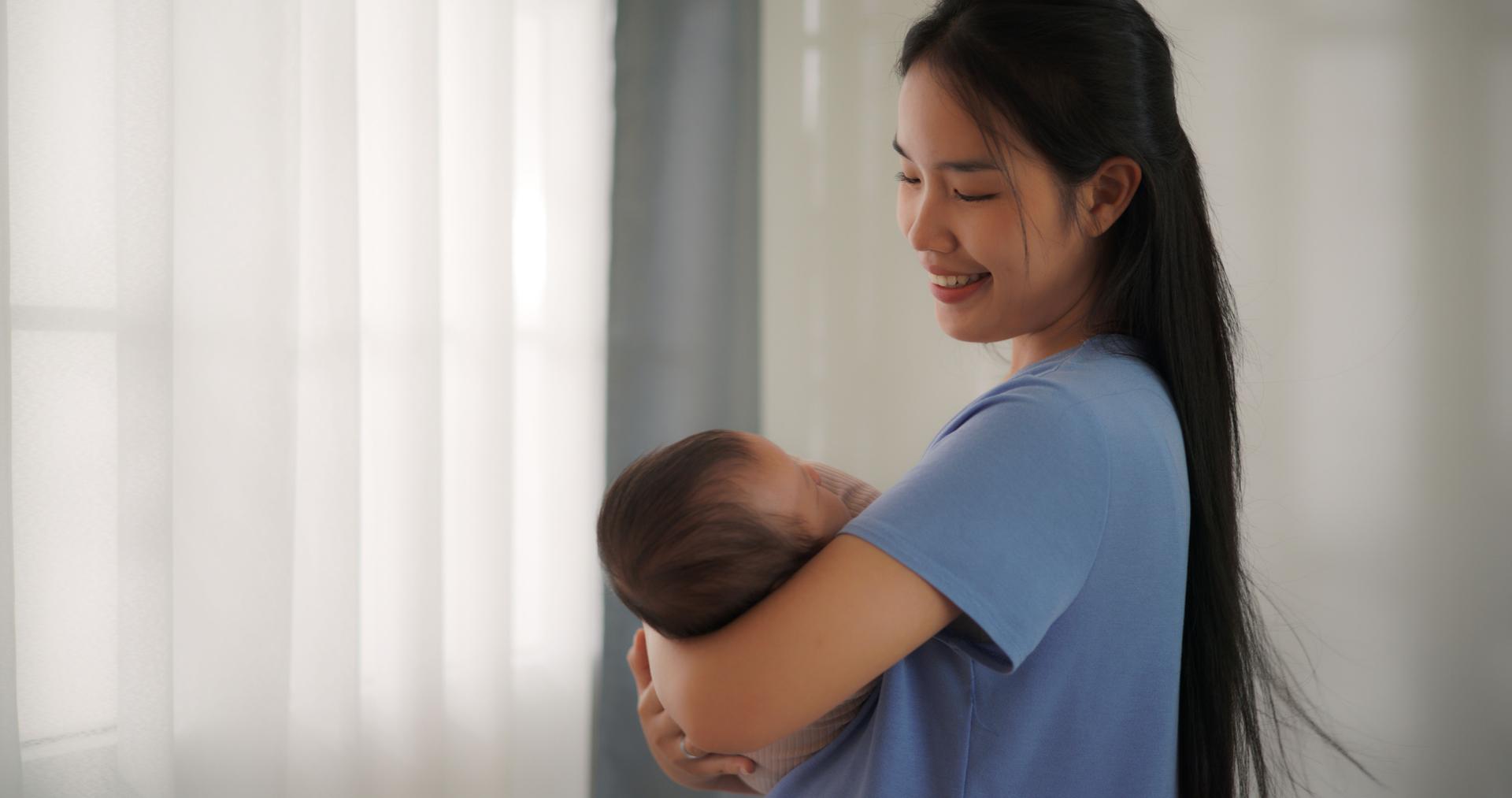 Happy mother holding baby boy on arm and looks at his with love and care.