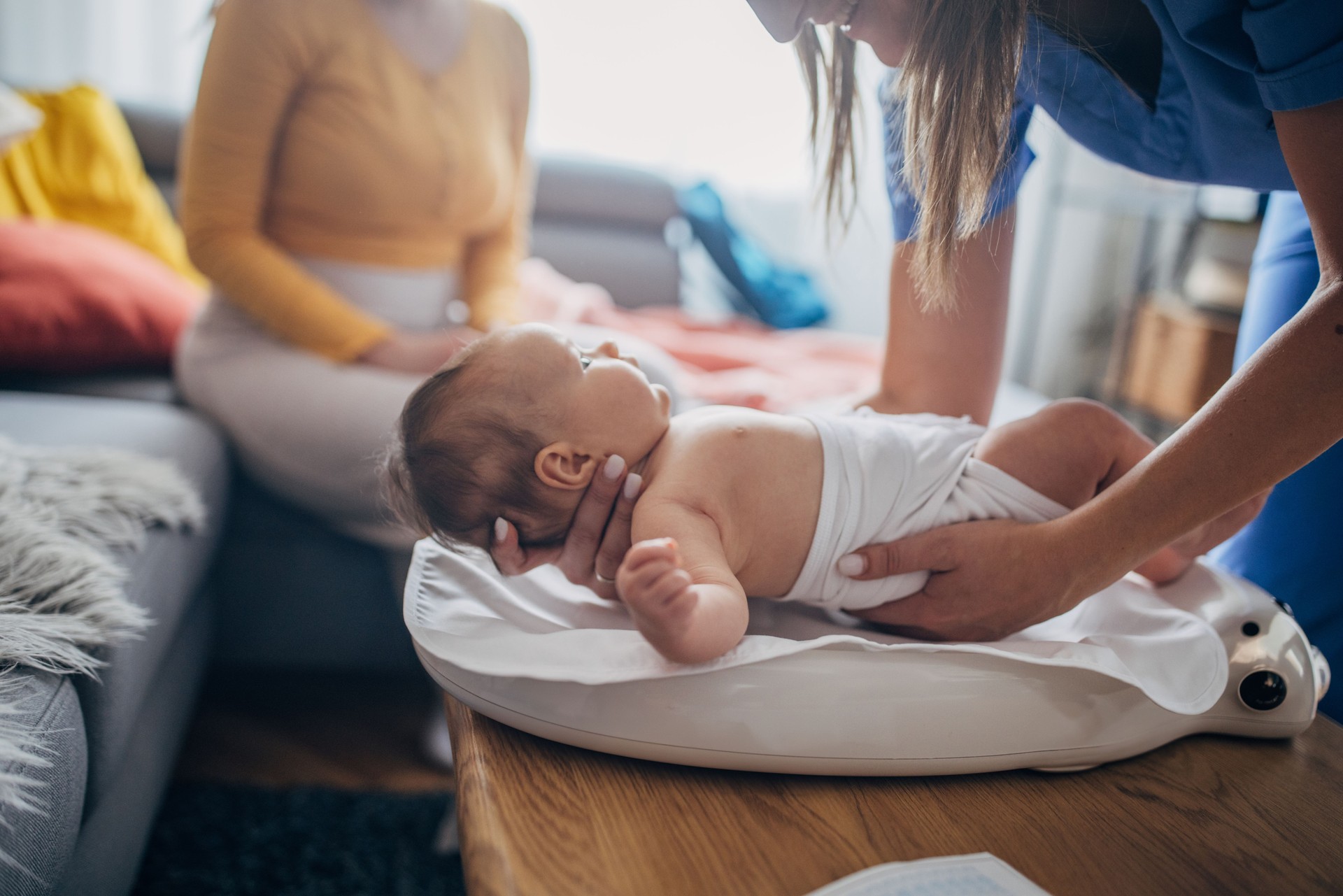 Female doctor at house visit,checking up newborn baby girl